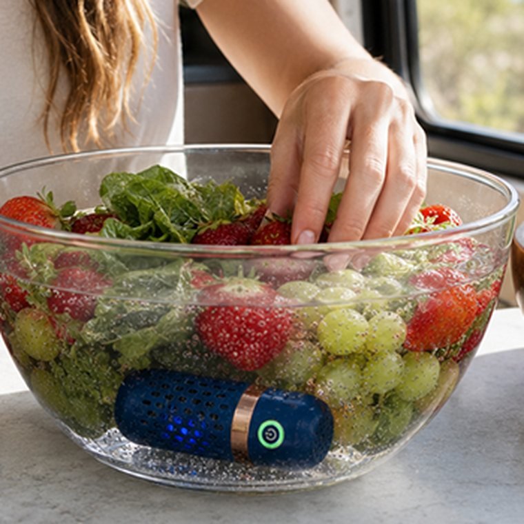 A hand placing fruit into a bowl of water with the PodBloom device running